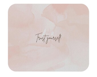 Peut inclure: Un tapis de souris carré avec un motif de style aquarelle dans des tons roses et blancs. Les mots "Trust yourself" sont écrits dans une police cursive délicate au centre du tapis de souris.