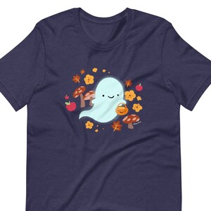 Pu&ograve; includere: Una maglietta blu navy con un simpatico fantasma dei cartoni animati che tiene un secchiello di zucca. Il fantasma &egrave; circondato da foglie autunnali, funghi e mele.