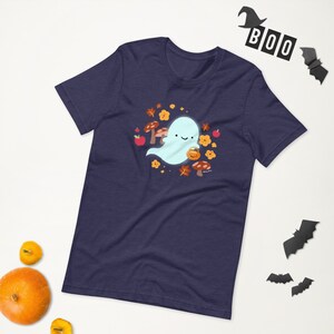 Pu&ograve; includere: Una maglietta blu navy con un simpatico fantasma che tiene una zucca. Il fantasma &egrave; circondato da foglie autunnali, funghi e mele.
