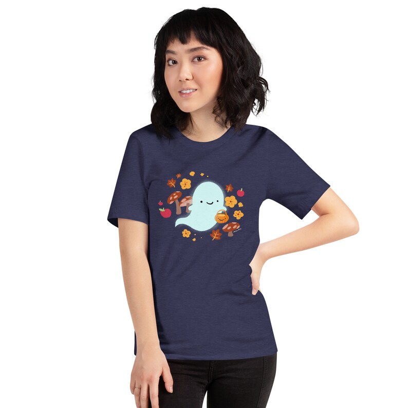 Pu&ograve; includere: Una maglietta blu navy con un simpatico fantasma che tiene una zucca. Il fantasma &egrave; circondato da foglie autunnali, funghi e mele.
