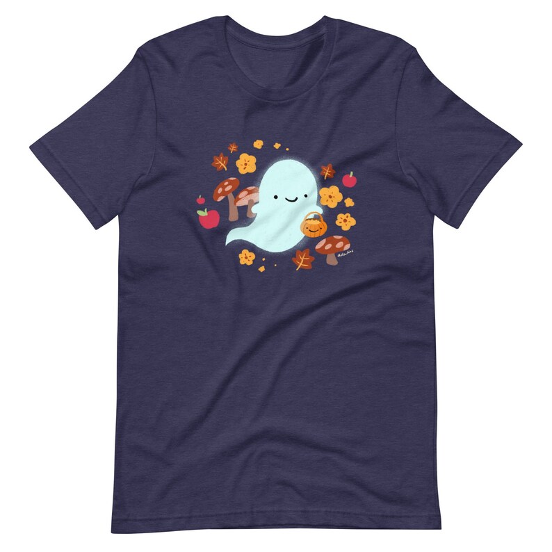 Pu&ograve; includere: Una maglietta blu navy con un simpatico fantasma dei cartoni animati che tiene un secchiello di zucca. Il fantasma &egrave; circondato da foglie autunnali, funghi e mele.