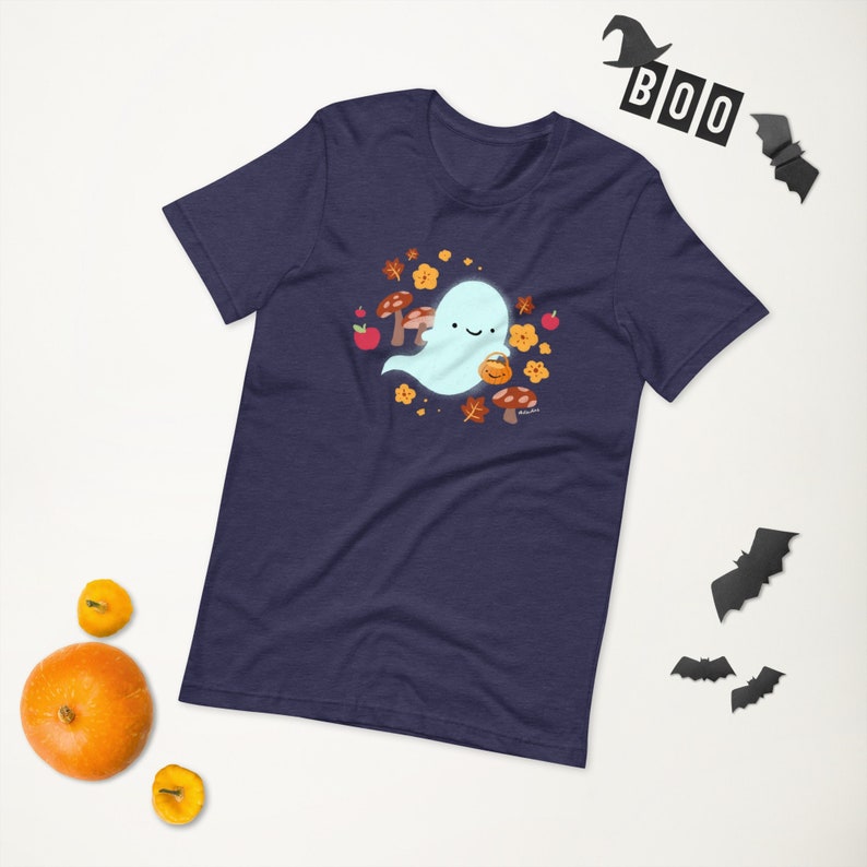 Pu&ograve; includere: Una maglietta blu navy con un simpatico fantasma che tiene una zucca. Il fantasma &egrave; circondato da foglie autunnali, funghi e mele.