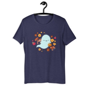 Pu&ograve; includere: Una maglietta blu navy con un simpatico fantasma dei cartoni animati che tiene un secchiello di zucca. Il fantasma &egrave; circondato da foglie autunnali, funghi e mele.