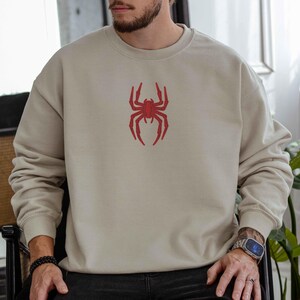 May include: A beige sweatshirt with a red spider graphic on the front.