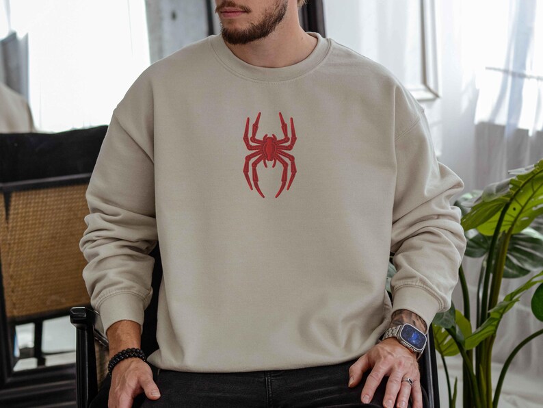 May include: A beige sweatshirt with a red spider graphic on the front.