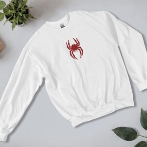May include: White sweatshirt with a red spider graphic on the front.
