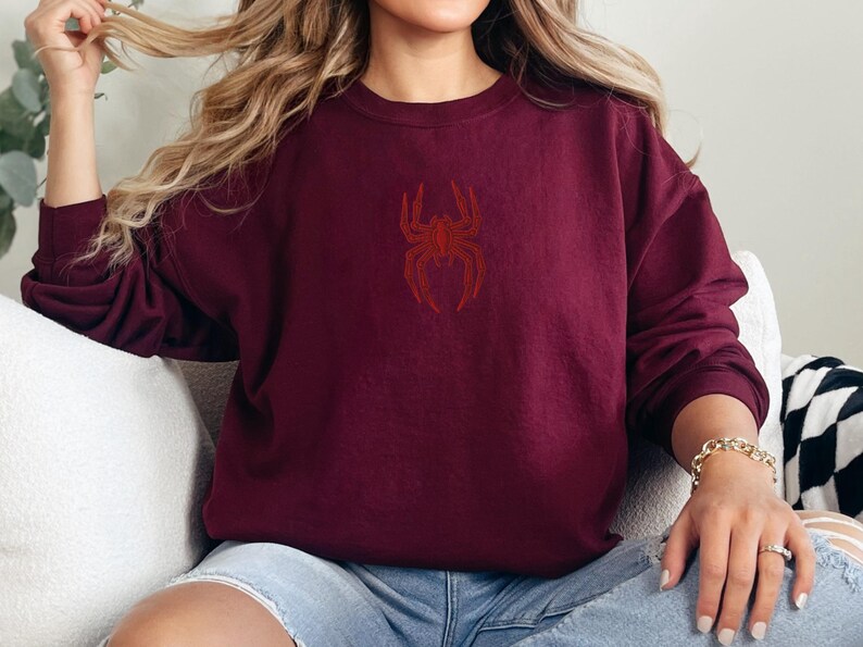May include: A maroon sweatshirt with a red embroidered spider design on the front.