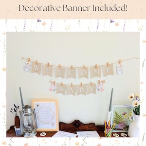 May include: A decorative banner with the words "WELCOME BABY" is strung across a wall. The banner is made of tan pennants with white letters, and is decorated with baby-themed illustrations. The image also includes a framed print and other decorative items.