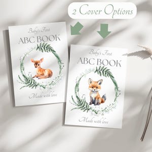Peut inclure: Deux livres ABC pour b&eacute;b&eacute;s avec des couvertures diff&eacute;rentes. L'un pr&eacute;sente un faon, l'autre un renard, tous deux dans une couronne verte. Le texte indique "Baby's First ABC BOOK" et "Made with love". L'image montre &eacute;galement "2 Cover Options".