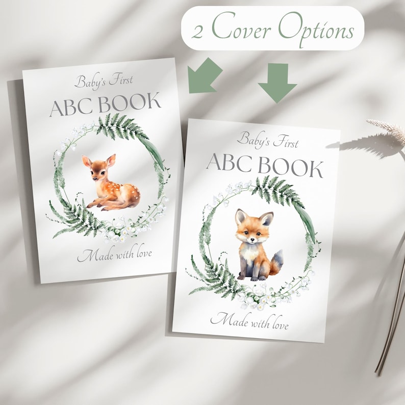 Peut inclure: Deux livres ABC pour b&eacute;b&eacute;s avec des couvertures diff&eacute;rentes. L'un pr&eacute;sente un faon, l'autre un renard, tous deux dans une couronne verte. Le texte indique "Baby's First ABC BOOK" et "Made with love". L'image montre &eacute;galement "2 Cover Options".