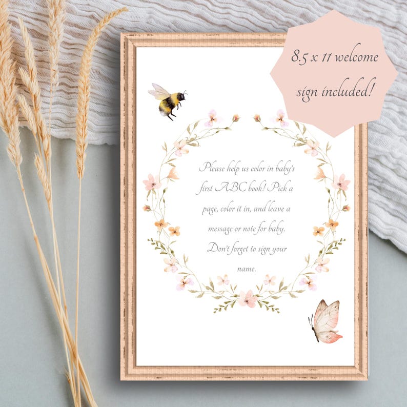 May include: A framed 8.5 x 11 welcome sign with a floral wreath and watercolor illustrations of a bee and butterfly. The sign includes text that reads, "Please help us color in baby's first ABC book!" and invites guests to leave a message.