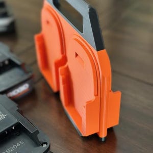 Pode incluir: Suporte para baterias laranja e preto com al&ccedil;a. O suporte tem duas ranhuras para baterias. O texto "CS2045" &eacute; vis&iacute;vel em uma bateria preta.