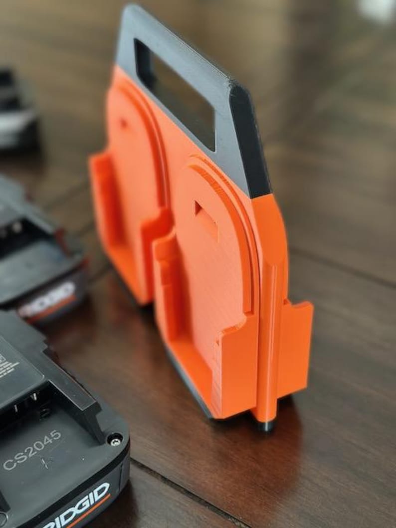 Pode incluir: Suporte para baterias laranja e preto com al&ccedil;a. O suporte tem duas ranhuras para baterias. O texto "CS2045" &eacute; vis&iacute;vel em uma bateria preta.
