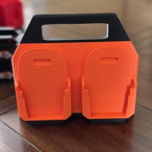 Pode incluir: Esta&ccedil;&atilde;o de carregamento impressa em 3D laranja e preta com duas ranhuras para carregar dispositivos.