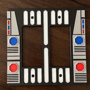 May include: A black and white light switch cover with a geometric design. The cover has a red, white, and blue accent on the side.
