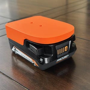 May include: An orange and black Ridgid 18V lithium-ion battery with a 2Ah capacity. The battery has a digital display that shows the charge level.