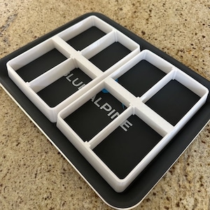 May include: White plastic mold with six rectangular compartments. The mold is on a black surface.