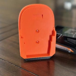 May include: Orange plastic battery holder with a black base. The holder has three holes and a rectangular cutout on the back.