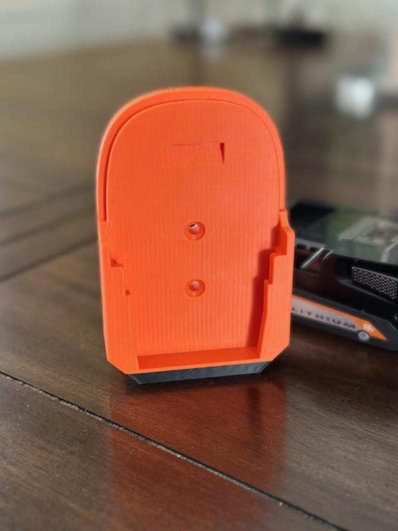 May include: Orange plastic battery holder with a black base. The holder has three holes and a rectangular cutout on the back.