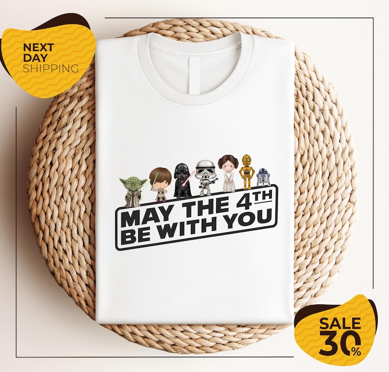 A white t-shirt with a graphic design featuring characters from the Star Wars franchise, along with the text "May the 4th be with you".