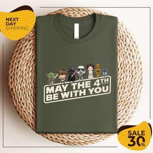 A green t-shirt with a graphic design featuring characters from the Star Wars franchise, along with the text "May the 4th be with you".
