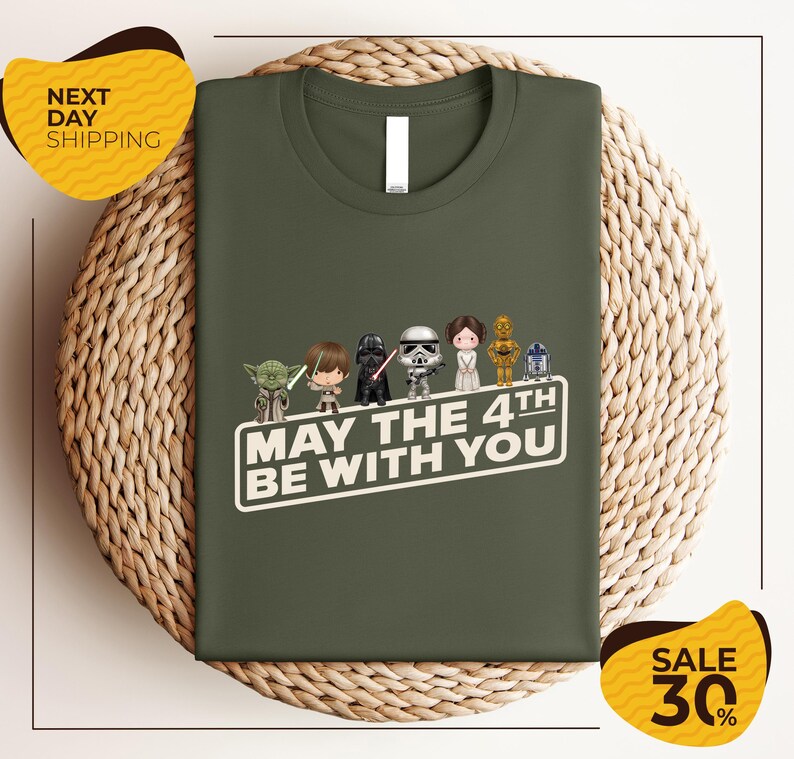 A green t-shirt with a graphic design featuring characters from the Star Wars franchise, along with the text "May the 4th be with you".