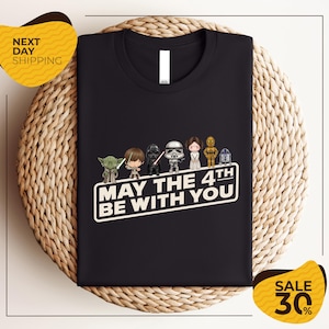 A black t-shirt with a graphic design featuring various characters from the Star Wars franchise, along with the text "May the 4th be with you".
