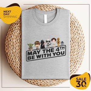 A gray t-shirt with a graphic design featuring characters from the Star Wars franchise, along with the text "May the 4th be with you".