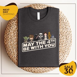 A gray t-shirt with a graphic design featuring characters from the Star Wars franchise, along with the text "May the 4th be with you".