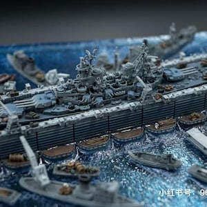 May include: A detailed model of a battleship with intricate detailing, surrounded by smaller boats, set in a sea-like environment. The model is primarily gray with blue accents, showcasing a miniature naval scene.