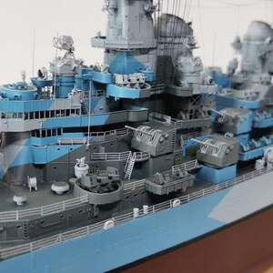May include: A detailed model of a battleship, painted in shades of blue, gray, and white. The model features multiple turrets, gun emplacements, and intricate detailing on the deck and superstructure. The hull is a dark brown color.