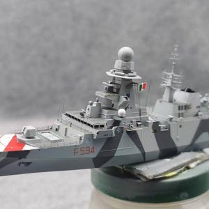 May include: A detailed model of a warship, painted in shades of gray with a camouflage pattern. The bow features red and white stripes. The model has a radar dome and the number F594.