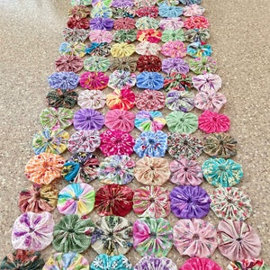 May include: A long table runner made of colorful fabric circles. The circles are sewn together to create a patchwork design. The runner is perfect for adding a touch of whimsy to any table.