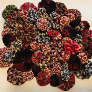 May include: A collection of fabric scraps sewn together to create a variety of small, round, quilted flowers. The flowers are in shades of red, green, black, and white.