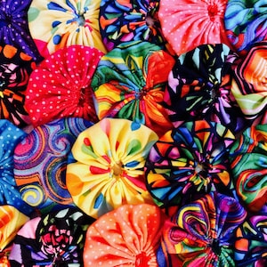 May include: A collection of colorful fabric flowers with various patterns, including polka dots, swirls, and geometric designs. The flowers are all made with a gathered fabric technique, creating a 3D effect.