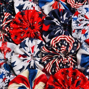 May include: A collection of fabric scraps sewn together in a circular pattern. The fabric is red, white, and blue with stars and stripes. The fabric is arranged in a circular pattern, with the center of the circle being the most prominent.
