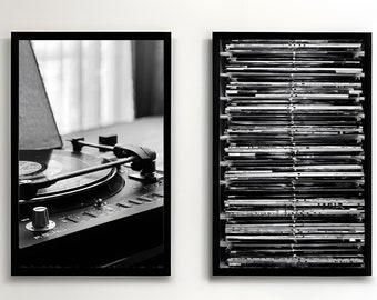 May include: Two black framed pictures on a white wall, one with a vintage record player and the other with a stack of vinyl records. Two black leather armchairs with wooden arms are in front of the pictures, and a small gold table with a green plant sits between them.