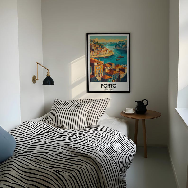 May include: A black and white striped bedspread with two matching pillows on a bed in a small room. A framed poster of Porto, Portugal hangs on the wall above the bed. A small wooden side table with a black pitcher and a cup sits next to the bed.