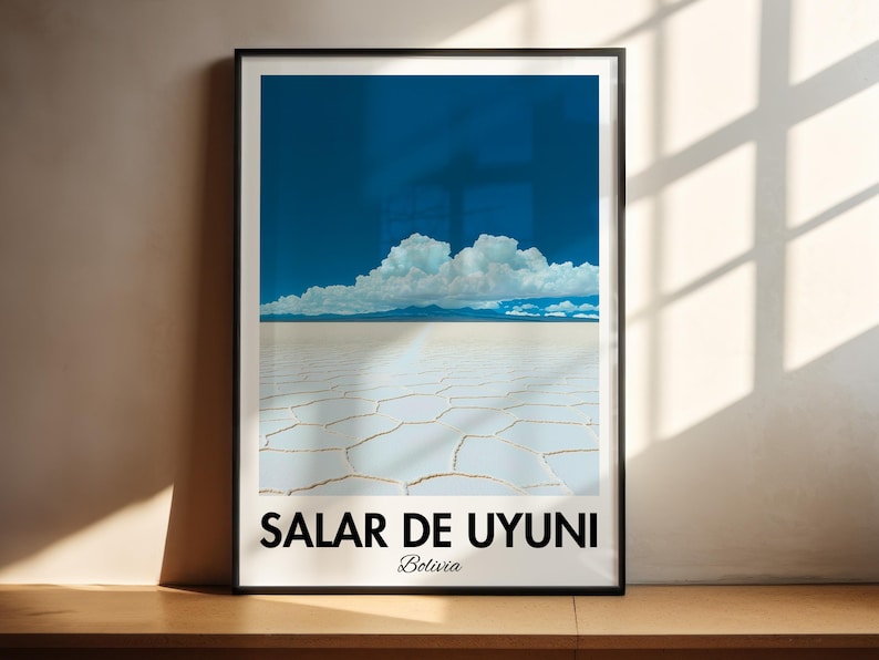 Op de afbeelding: Een ingelijste poster met een foto van de Salar de Uyuni zoutvlakte in Bolivia. De foto toont een uitgestrekt, wit, gebarsten oppervlak met een enkele wolk in de blauwe lucht erboven. De poster heeft de tekst "Salar de Uyuni" en "Bolivia" in zwart gedrukt aan de onderkant.
