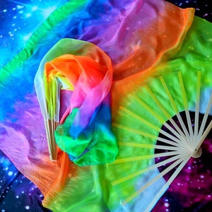 Peut inclure: Un foulard en soie aux couleurs de l'arc-en-ciel avec un &eacute;ventail en bois. Le foulard est pli&eacute; et drap&eacute; sur un fond bleu fonc&eacute; avec des &eacute;toiles blanches.