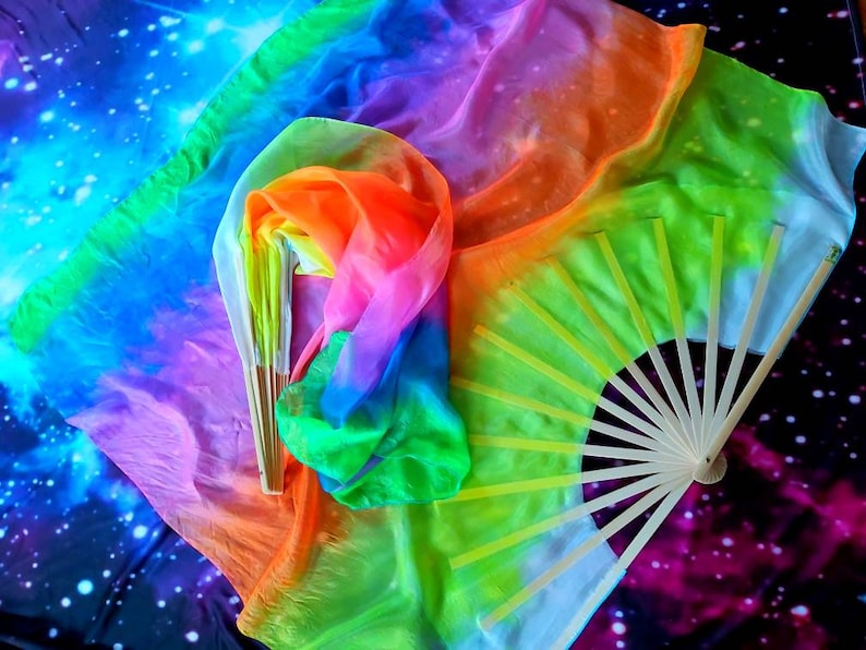 Peut inclure: Un foulard en soie aux couleurs de l'arc-en-ciel avec un &eacute;ventail en bois. Le foulard est pli&eacute; et drap&eacute; sur un fond bleu fonc&eacute; avec des &eacute;toiles blanches.