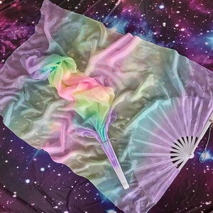 May include: A rainbow-coloured silk fabric fan with a white handle. The fan is laid out on a dark purple background with white stars.