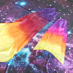 May include: Two flowy fabric dance veils featuring a vibrant gradient pattern that transitions from deep purple at the top to magenta, orange, and bright yellow at the bottom edges. The lightweight material has a soft, semi-sheer texture.