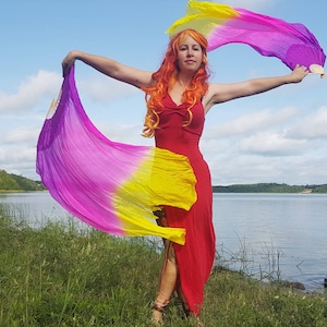 May include: A pair of silk fan veils featuring a vibrant gradient of yellow, hot pink, and purple. The fabric is attached to a lightweight, foldable wooden frame, allowing the long, flowing material to extend outward in a wide, colourful arc.