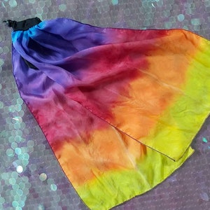 May include: A flowing fabric accessory featuring a vibrant gradient of colours transitioning from deep purple to magenta, orange, and bright yellow. The piece is gathered at one end with a black cord lock mechanism, creating a soft, draped effect.