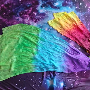 May include: Two dance flags made of lightweight fabric. The larger flag features a gradient of green, blue, and purple. The smaller flag displays a gradient of yellow, orange, and red. Both flags have small, round, coloured beads attached at the base.
