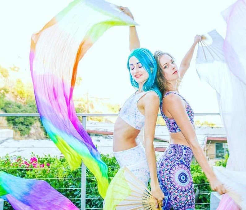 Peut inclure: Deux personnes tiennent des rubans de tissu color&eacute;s et des &eacute;ventails. La personne &agrave; gauche a les cheveux bleus et porte un haut court et un pantalon blancs. La personne &agrave; droite a les cheveux bruns et porte un haut court et un pantalon &agrave; motifs bleus et blancs.