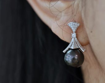May include: A pair of silver earrings with a black pearl drop and a diamond-encrusted design.