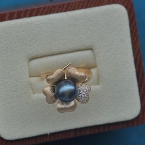 May include: A gold ring with a black pearl and clear stones set in a four-leaf clover design.