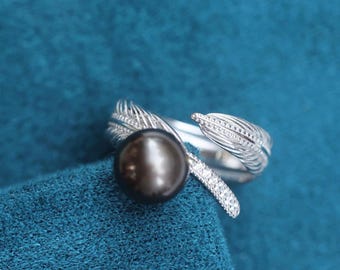 May include: A silver ring with a black pearl and a feather design. The ring is set with small clear stones.